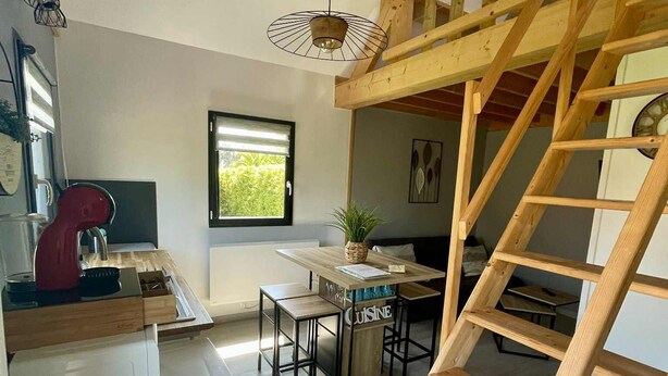 Una cocina con una escalera de madera, un comedor con mesa y sillas, y un ventanal con persianas.