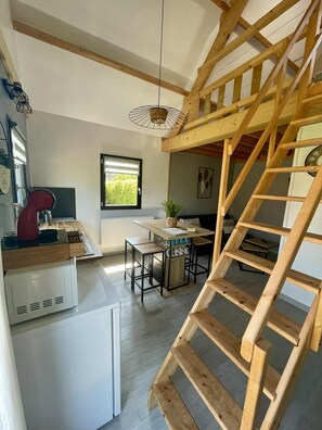 A kitchen with a wooden staircase, a dining area with a table and chairs, and a window with blinds. - Chalet with a Jacuzzi; pets welcome   (Port-Bail-sur-Mer)