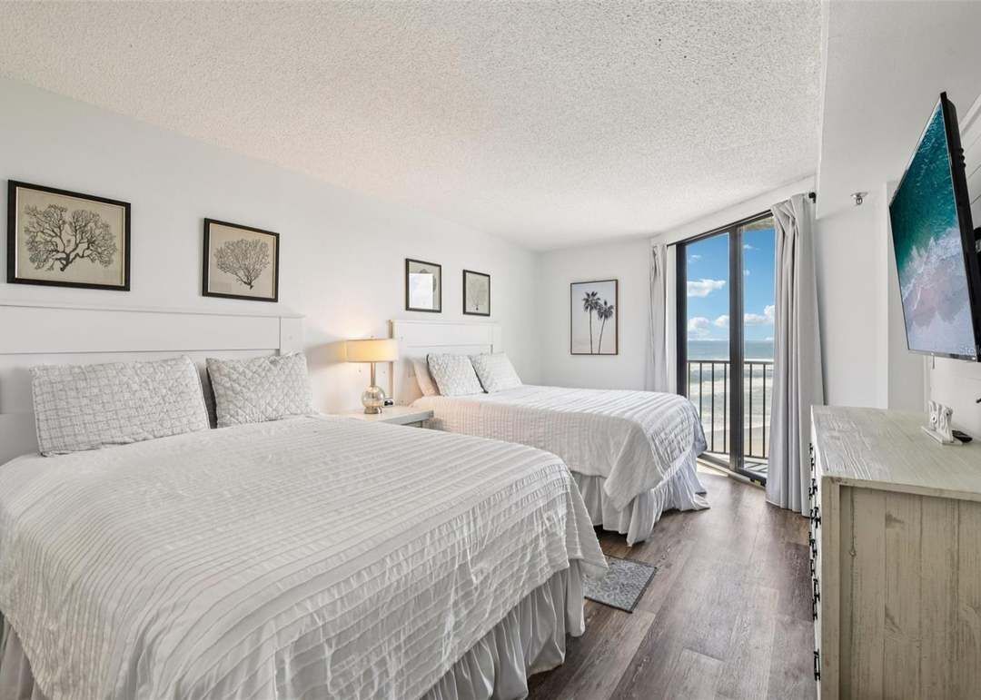 A hotel room with two beds, a desk, and a large window with a view.