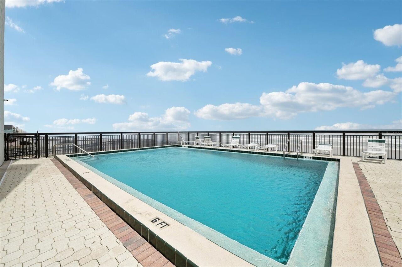 Ein rechteckiger Swimmingpool mit einer Tiefenmarkierung von 6 Fuß, umgeben von einem schwarzen Metallzaun und weißen Liegestühlen.