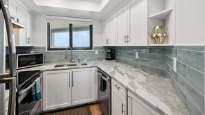 A modern kitchen with white cabinets, a built-in microwave, and a coffee maker.