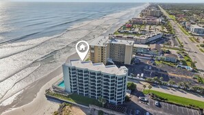 An aerial view of a coastal hotel with multiple buildings, a swimming pool, and a beach in the background.