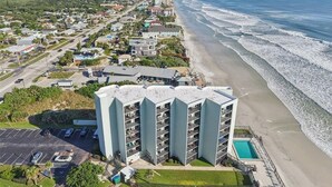 A multi-story hotel with a pool, located near a beach with ocean views.