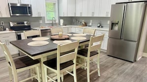 A modern kitchen with white cabinets, stainless steel appliances, and a wooden dining table with four chairs. - BlueSky on the Cape Fear River (Burgaw)