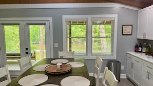 A dining area with a wooden table, white chairs, and a kitchen area with cabinets and a countertop. - BlueSky on the Cape Fear River (Burgaw)