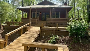 A wooden cabin with a porch, surrounded by a forest. - BlueSky on the Cape Fear River (Burgaw)