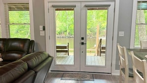 A living room with a dark leather couch, a wooden dining table with chairs, and a sliding glass door leading to an outdoor deck. - BlueSky on the Cape Fear River (Burgaw)