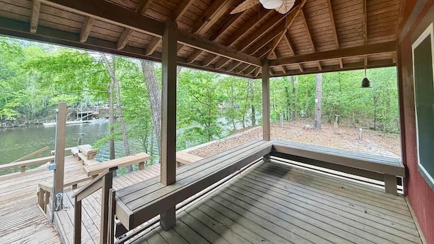A covered wooden deck with a ceiling fan, benches, and a view of a lake surrounded by trees. - BlueSky on the Cape Fear River (Burgaw)
