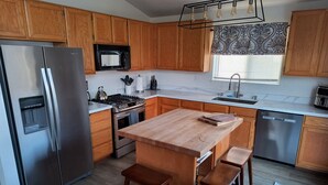 Een moderne keuken met houten kastjes, roestvrijstalen apparatuur, een centraal eiland met krukken en een raamdecoratie met een patroon.