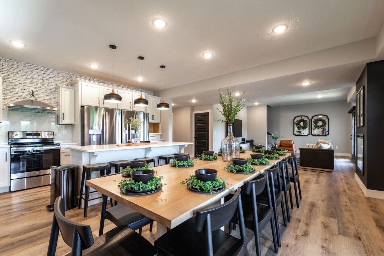 A modern kitchen with stainless steel appliances, a wooden dining table with black chairs, and pendant lighting.
