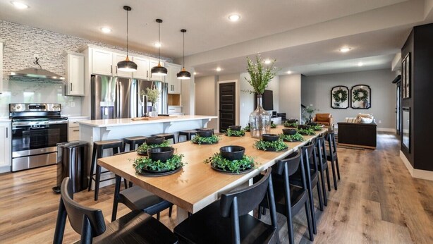 A modern kitchen with stainless steel appliances, a wooden dining table with black chairs, and pendant lighting.