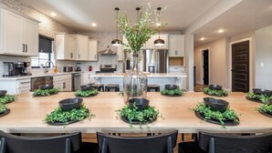 A modern kitchen with white cabinets, a central island with a vase, and black bowls with greenery.