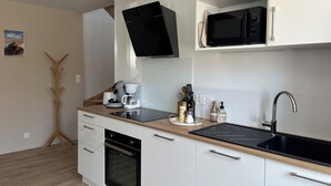 A modern kitchen with white cabinets, a black microwave, a coffee maker, and a sink. - Private SPA & Garden - 10 min from Mont St-Michel (Pontorson)