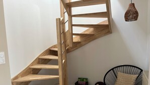 A wooden staircase with a black metal handrail, a black chair with a cushion, and a wicker pendant light. - Private SPA & Garden - 10 min from Mont St-Michel (Pontorson)
