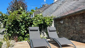 A wooden deck with two lounge chairs, surrounded by greenery and a stone wall. - Private SPA & Garden - 10 min from Mont St-Michel (Pontorson)