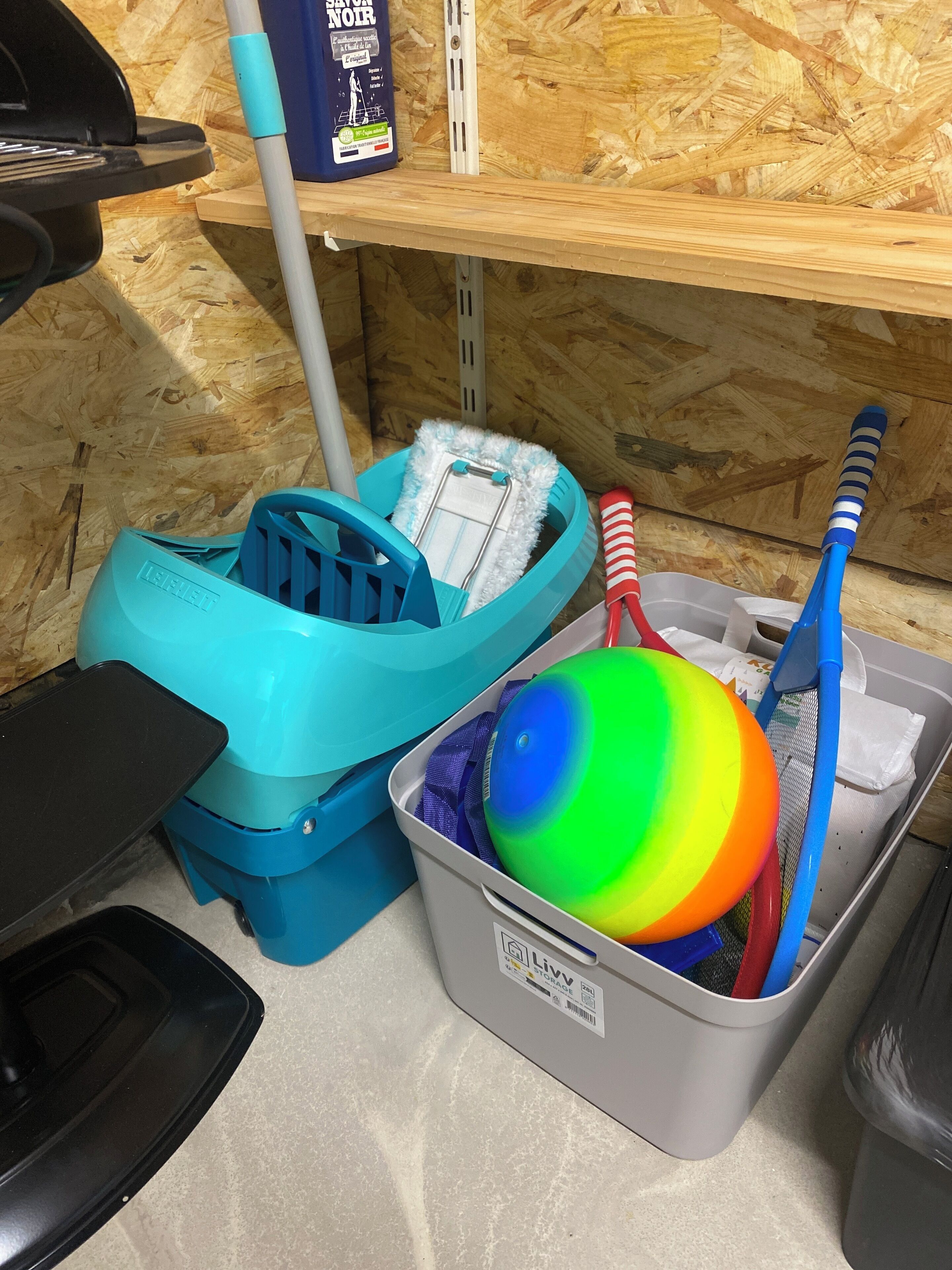Un área de almacenamiento con un contenedor de plástico azul que contiene una pelota colorida, un cepillo de dientes rojo y azul, y un recipiente blanco.