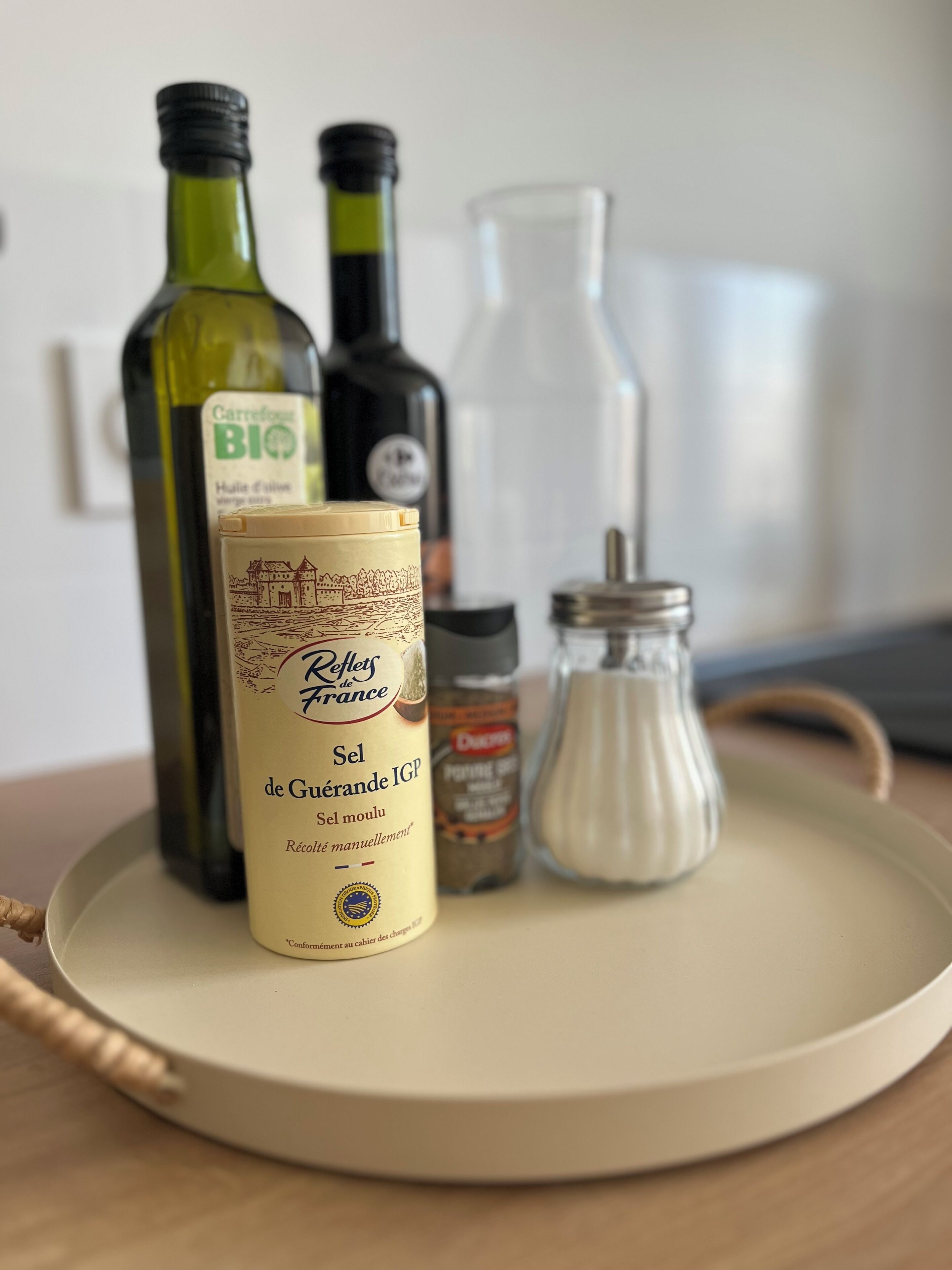 A tray with a bottle of Sel de Guérande IGP, a jar of Dijon mustard, a salt shaker, and two bottles of wine.