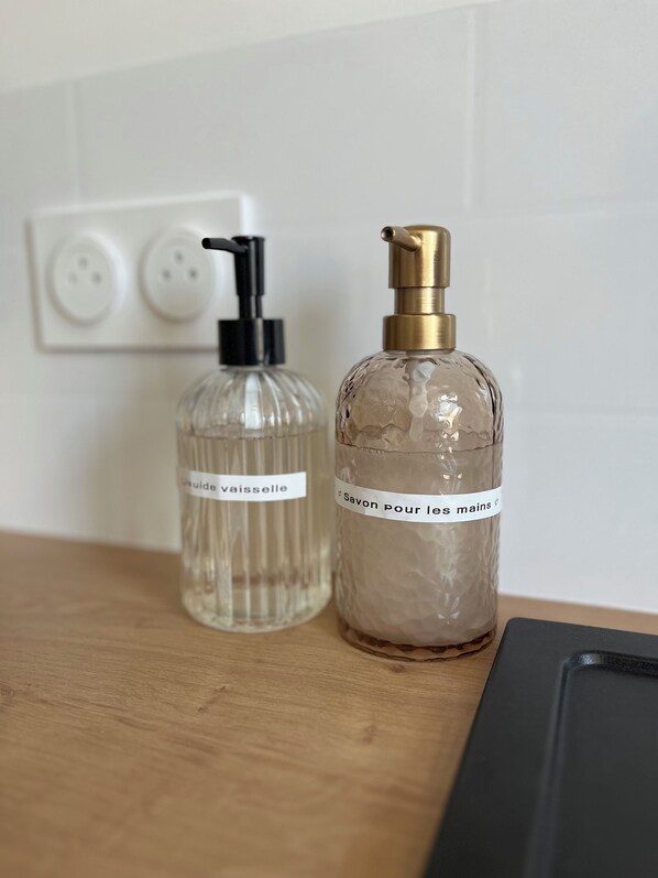 Two transparent bottles with pump dispensers on a wooden surface, one labeled 'Savon pour les mains' and the other 'Savon vaisselle'. - Private SPA & Garden - 10 min from Mont St-Michel (Pontorson)
