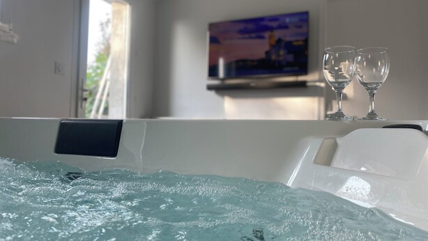 A hot tub with two glasses on the edge, a painting on the wall, and a window with daylight. - Private SPA & Garden - 10 min from Mont St-Michel (Pontorson)