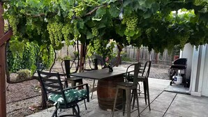Une terrasse avec une table et des chaises, un tonneau et une pergola couverte de vignes.