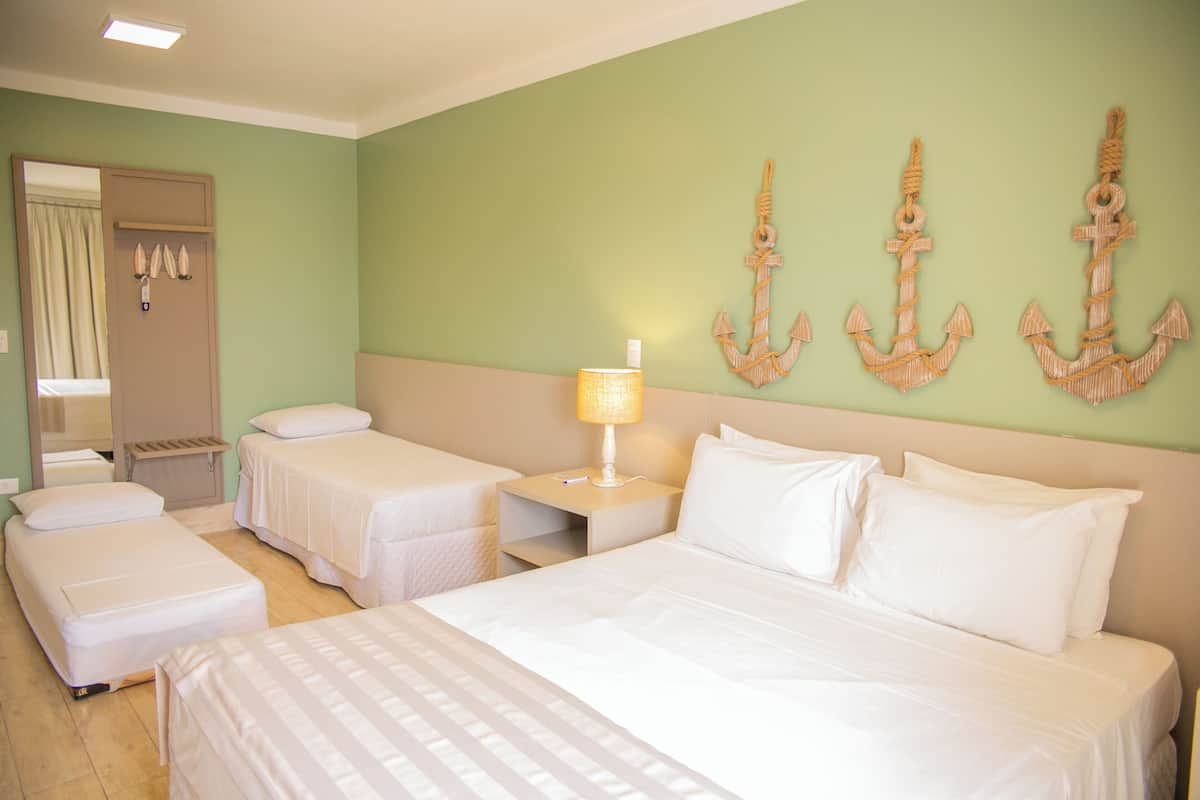 A hotel room with two single beds, a larger bed, a nightstand with a lamp, and decorative anchors on the wall.