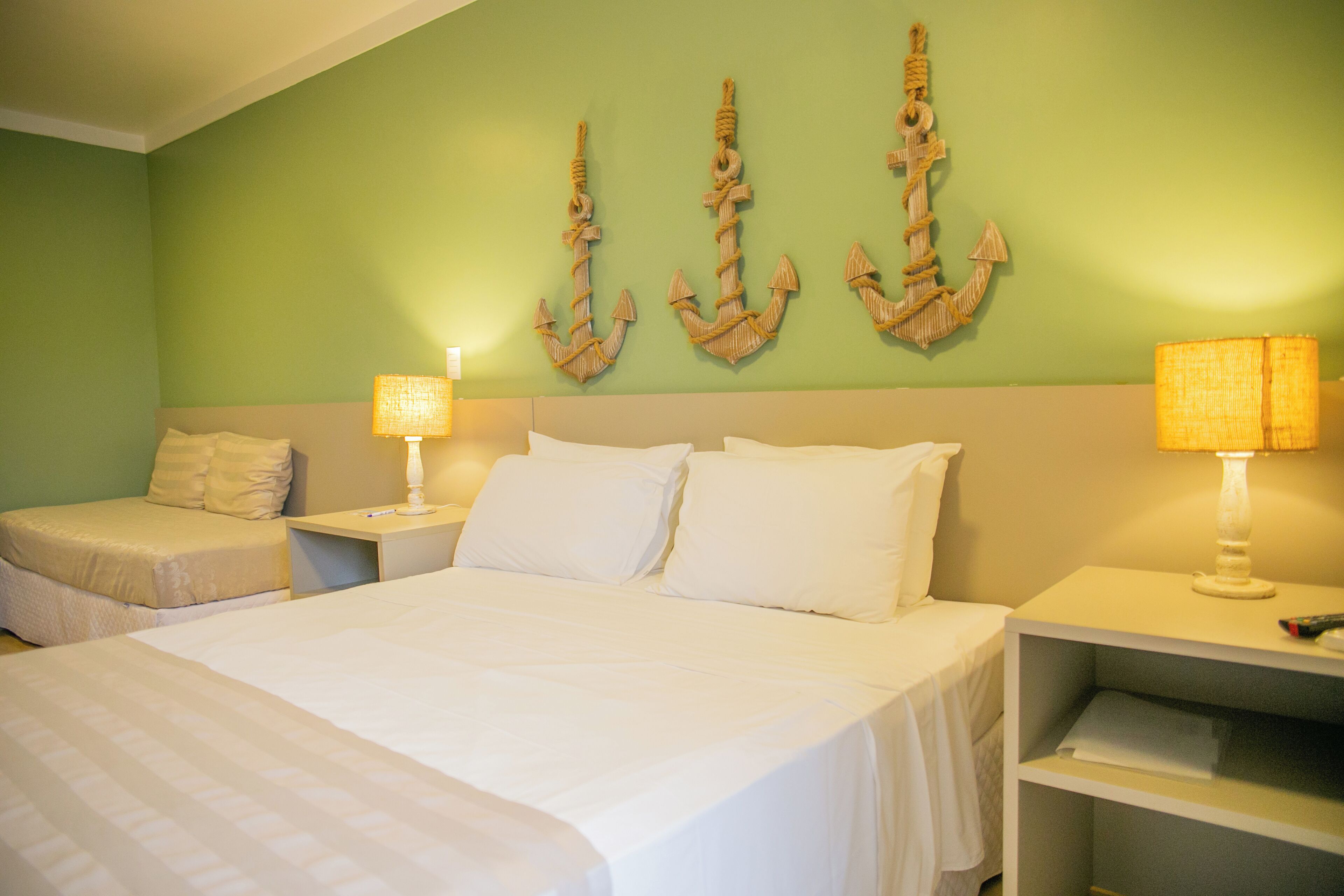 Quarto de hotel com uma cama grande, duas mesas de cabeceira com abajures, um sofá pequeno e três suportes fixados na parede.