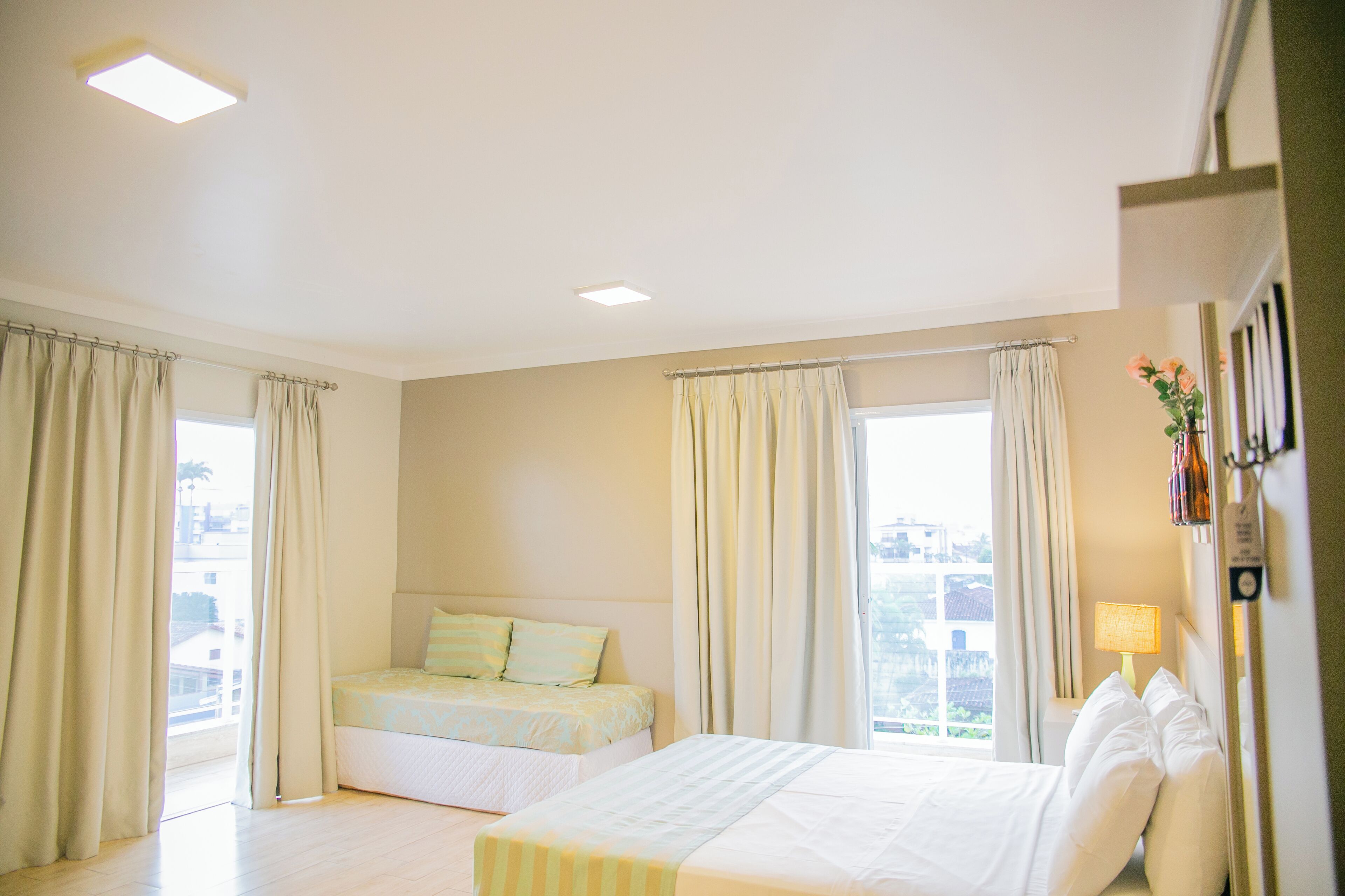 Quarto de hotel com duas camas, janelas amplas com cortinas, abajur e vista para a cidade.