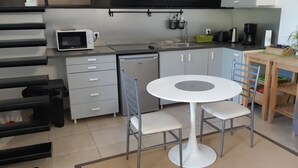 Cocina compacta equipada con microondas, tostadora y cafetera. Incluye una pequeña mesa de comedor con sillas y un sofá.