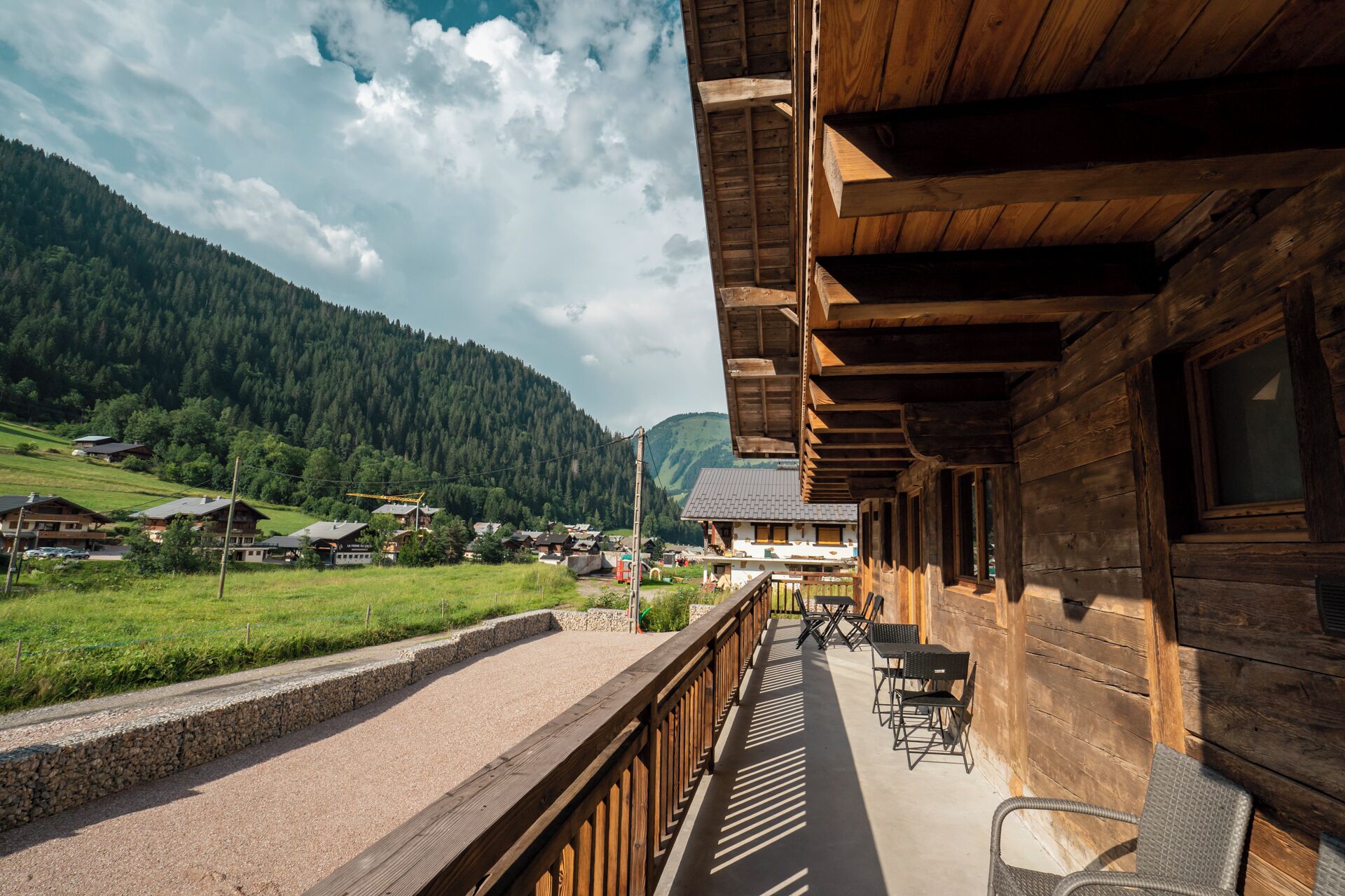 A wooden building with a balcony overlooking a rural landscape with houses and mountains.