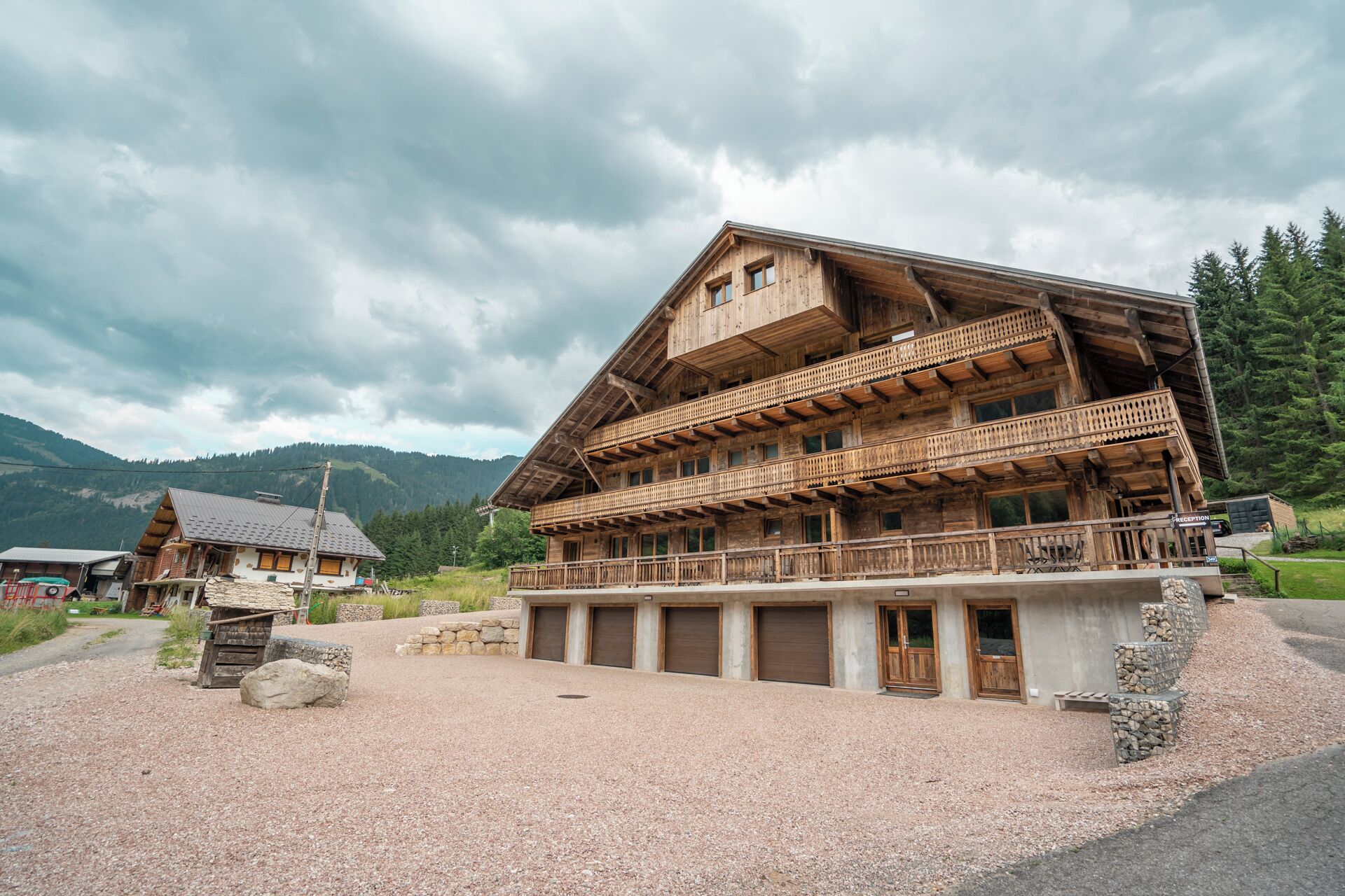 Ein traditionelles Holzchalet mit Balkon, Steinunterbau und einer Schotterzufahrt.