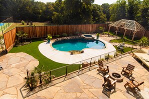 Un jardin avec une piscine, une terrasse en pierre, une terrasse en bois et une clôture en bois.