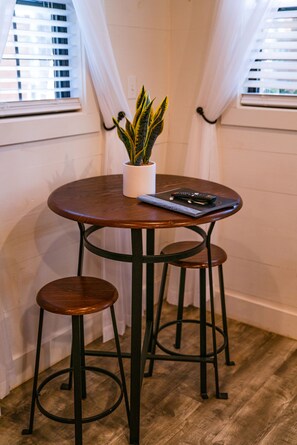 Une petite table ronde avec un pot de fleurs, deux tabourets et une télécommande.