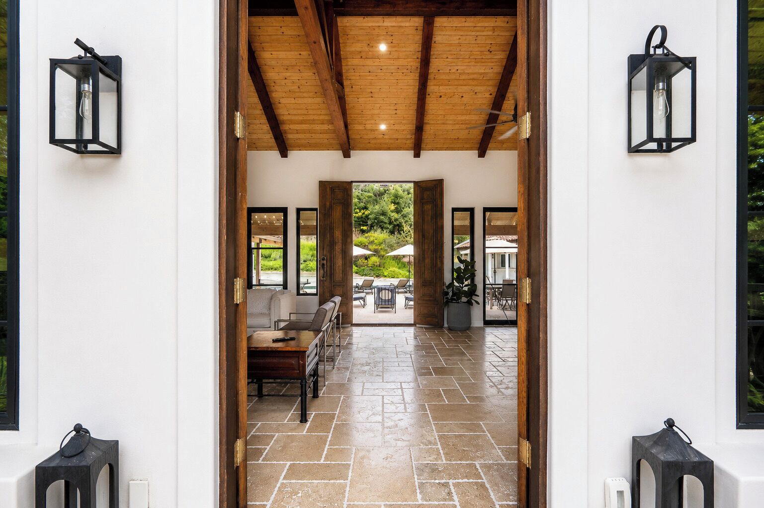 A doorway leading to an outdoor patio area with a stone floor, a seating arrangement, and two wall-mounted lanterns.