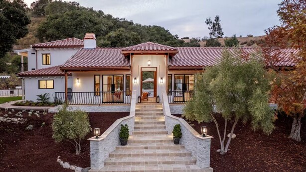 Una casa a due piani con tetto in tegole, un portico con gradini e un giardino curato.