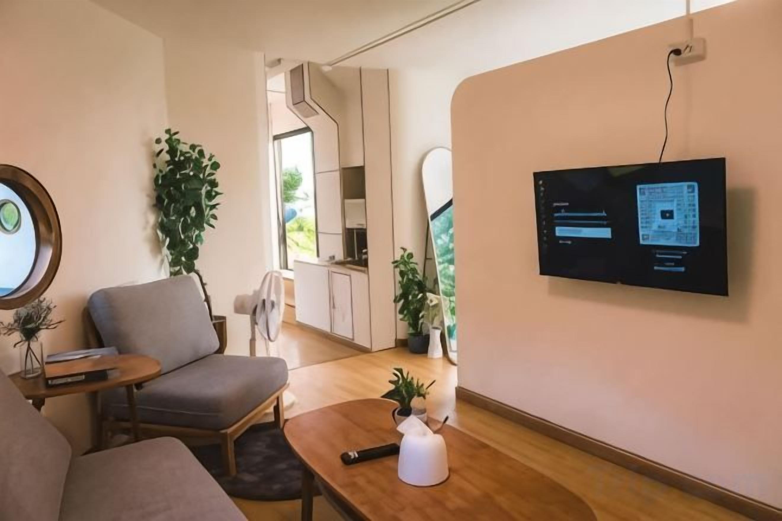 Una sala de estar moderna con un televisor de pantalla plana montado en la pared, un sofá, una mesa de centro con un jarrón y una silla.