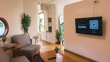 Una sala de estar moderna con un televisor de pantalla plana montado en la pared, un sofá, una mesa de centro con un jarrón y una silla.
