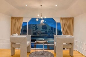 A room with two sofas, a small round table, a chandelier, and a large window with curtains.
