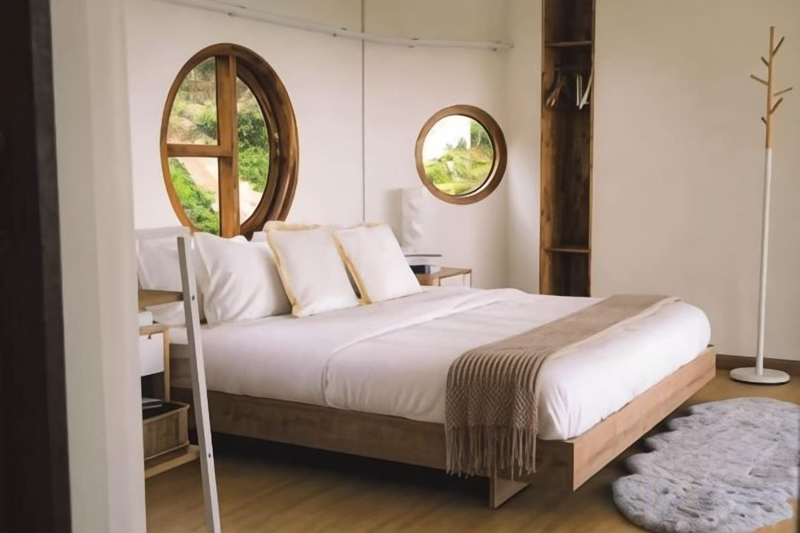 Un dormitorio con una cama de madera, dos mesitas de noche, un ventanal redondo y una lámpara de pie.