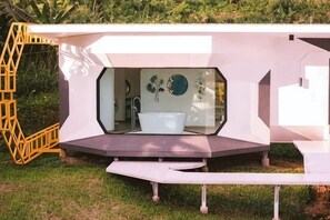Un baño moderno y geométrico con bañera, cerramiento de vidrio y una escalera amarilla.