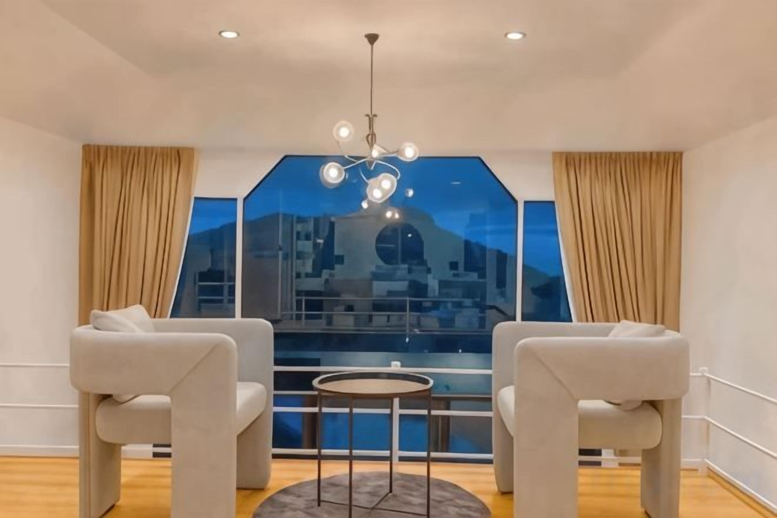 A room with two sofas, a small round table, and a large window with a view of a cityscape.