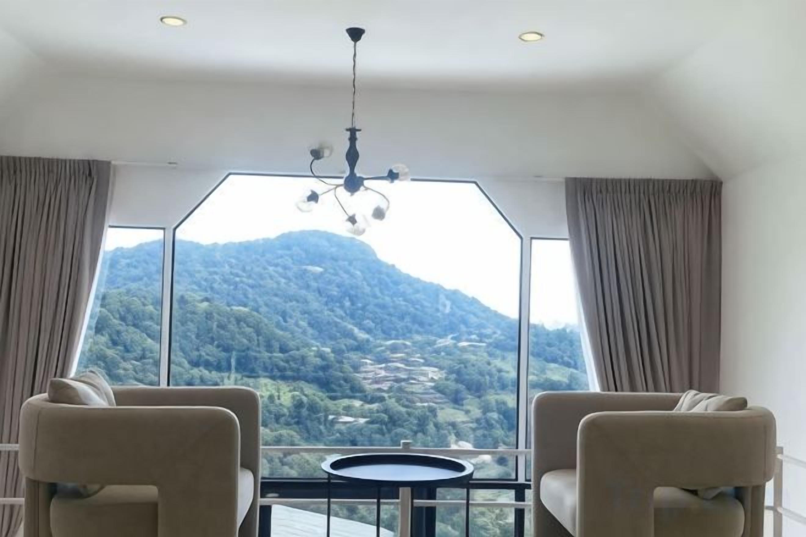 Una habitación con un ventanal amplio, dos sillas, una mesita y un candelabro.