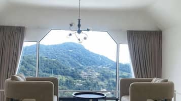 Una habitación con un ventanal amplio, dos sillas, una mesita y un candelabro.