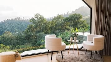 Una habitación con un ventanal grande, dos sillas blancas, una mesita y un tapete redondo.