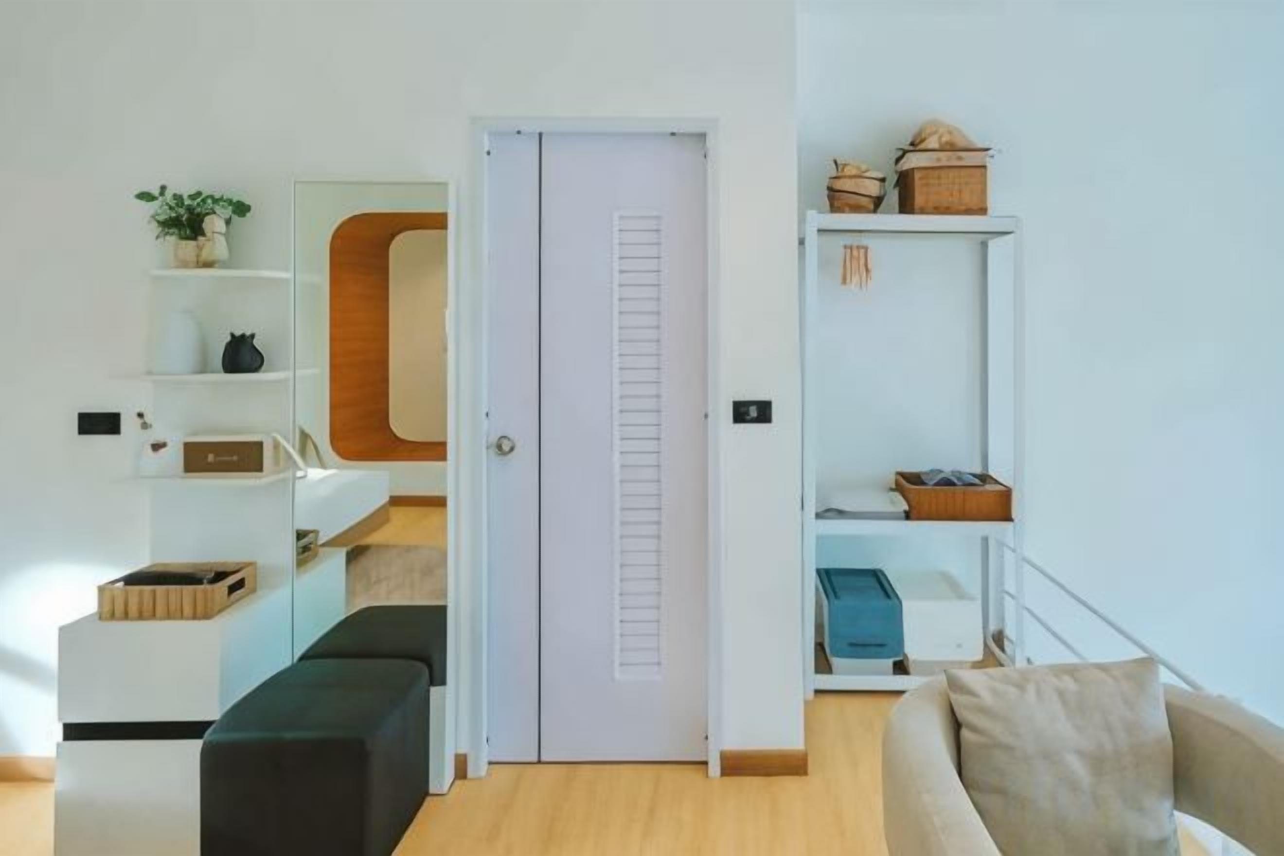 A modern living room with a sofa, a bench, a white door, and a shelving unit with various items.