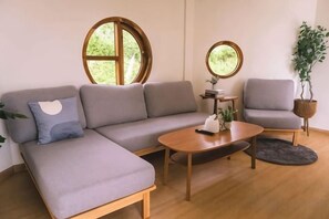 A modern living room with a grey sectional sofa, a round coffee table, and two armchairs. There are two round windows providing natural light. - SkyView Monjam (Mae Rim)