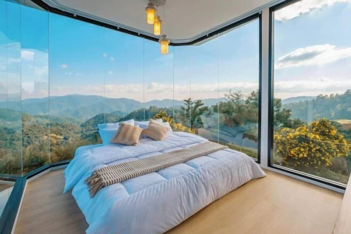 A bedroom with a large bed, a view of mountains, and a glass wall.
