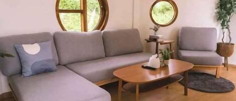 A modern living room with a grey sofa, a round coffee table, and a round window.
