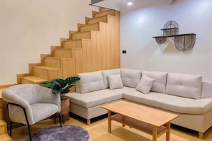 A living room with a sofa, a chair, a coffee table, a staircase, and a wall-mounted shelf.