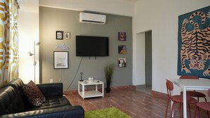 Ein Wohnzimmer mit einem schwarzen Ledersofa, einem weißen Couchtisch, einem an der Wand montierten Flachbildfernseher und einem Tigergemälde.