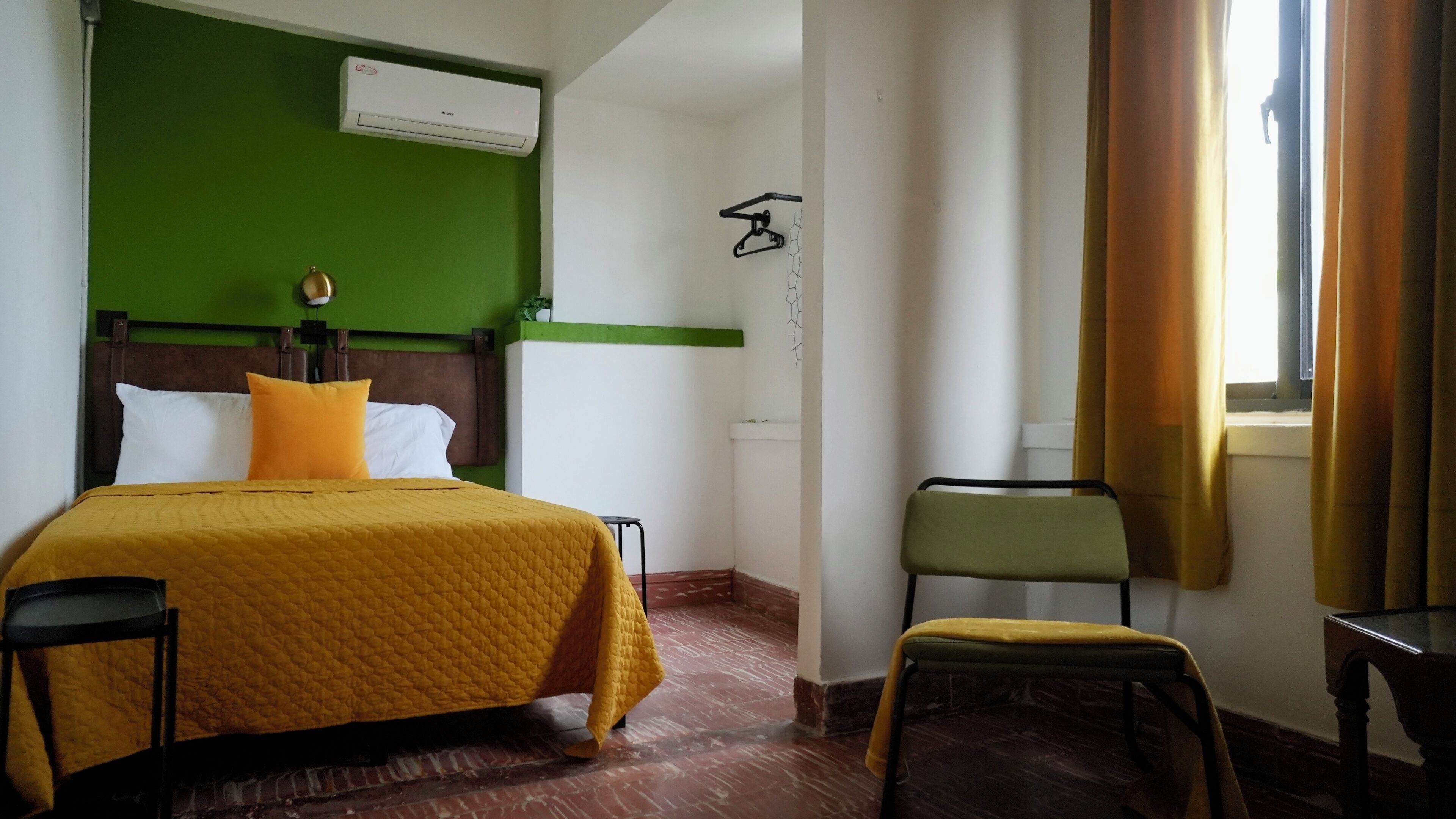Hotelkamer met een bed, een stoel, een tafeltje, een airconditioning en een raam met gordijnen.